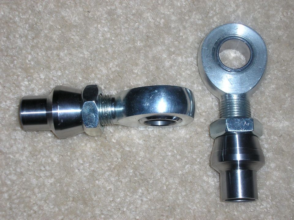 Two metal rod ends with hex nuts on threaded shafts, resting on a carpeted surface