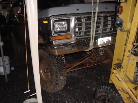 1979 Ford Bronco - Mud-covered 1979 Ford Bronco front end, partially obscured by a white pole and a yellow forklift.