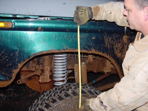 1979 Ford Bronco - A person uses a tape measure to check the suspension height of a mud-covered SUV.