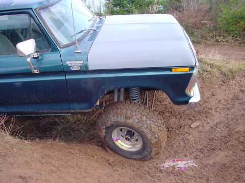 1979 Ford Bronco - Ford Bronco with lifted suspension and large tires navigating a muddy off-road trail.