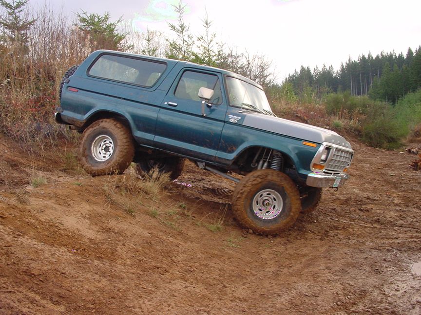 Teal 1979 Ford Bronco driving off-road on a muddy incline