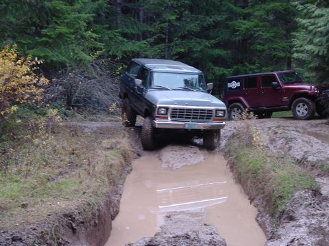 1979 Ford Bronco - A 1979 Ford Bronco navigates a challenging muddy trail, with another off-road vehicle visible in the background.