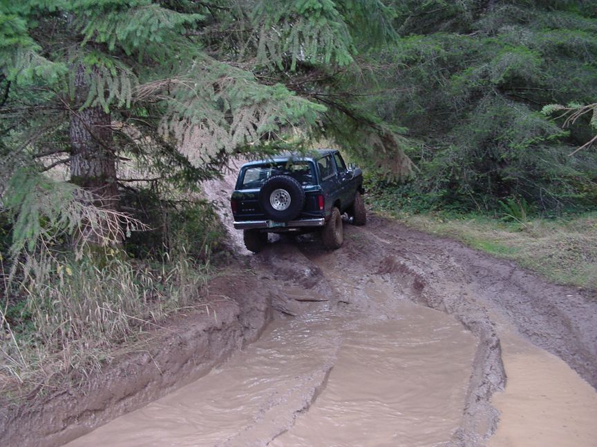 1979 Ford Bronco driving through a muddy trail in a forest