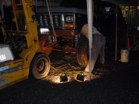1979 Ford Bronco - A person works on the front suspension of a Ford Bronco, which is being supported by a forklift.