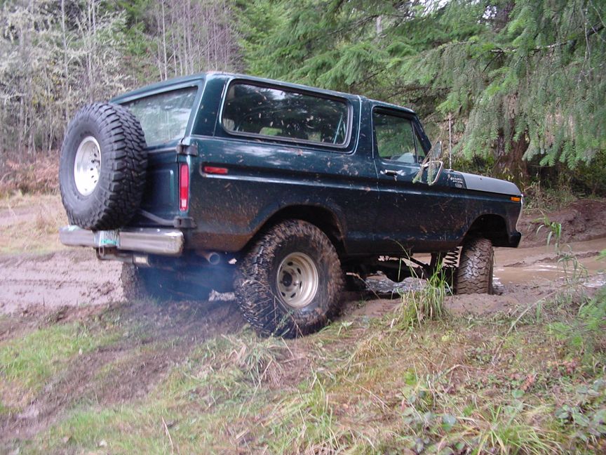 Dark green 1978 Ford Bronco with spare tire on back, stuck in mud with smoke coming from exhaust