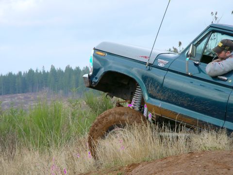 1979 Ford Bronco - A teal Ford Bronco is shown off-roading, with its front tire angled upwards on a dirt incline.