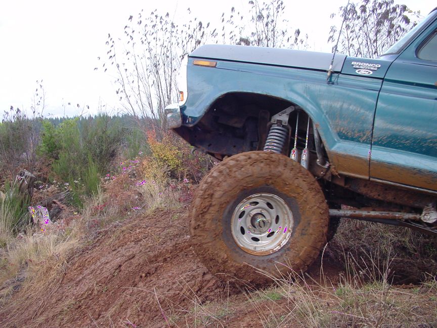 Green Ford Bronco with lifted suspension and large mud-covered tires driving off-road