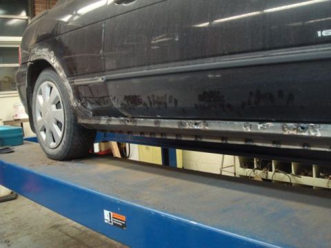 1996 Ford Bronco - The side panel of a black car shows significant rust and evidence of welding repairs on the rocker panel.