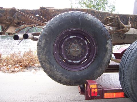 1996 Ford Bronco - The rear section of a heavily rusted truck frame is visible, along with a spare tire mounted on a trailer.
