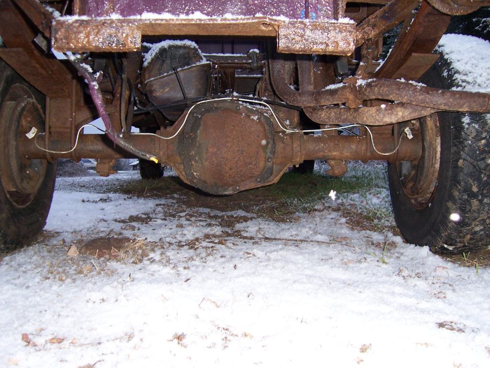 Rusty rear axle, leaf springs, and differential of an old truck in the snow