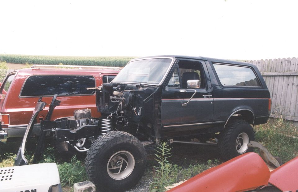 Dark blue Ford Bronco with front end removed, parked next to a red SUV