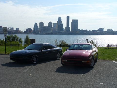 1991 Ford Probe - Two 1991 Ford Probes are parked near a waterfront with a city skyline in the background.