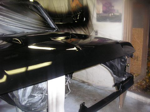 1987 Ford Bronco - A black vehicle hood and fender are shown during a painting process in a workshop.