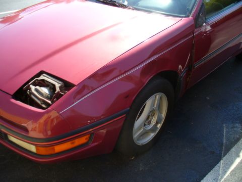 1991 Ford Probe - Close-up of a red 1991 Ford Probe's front fender and open headlight assembly.