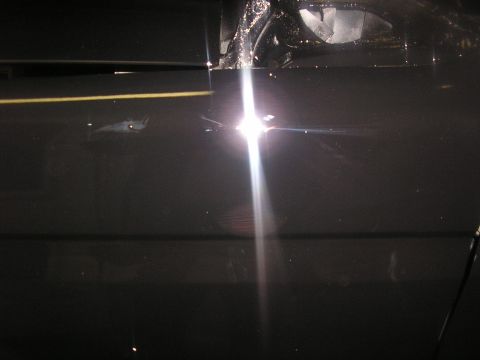 1987 Ford Bronco - Close-up of a black vehicle door showing a yellow stripe and a bright reflection, with a watermark at the bottom.