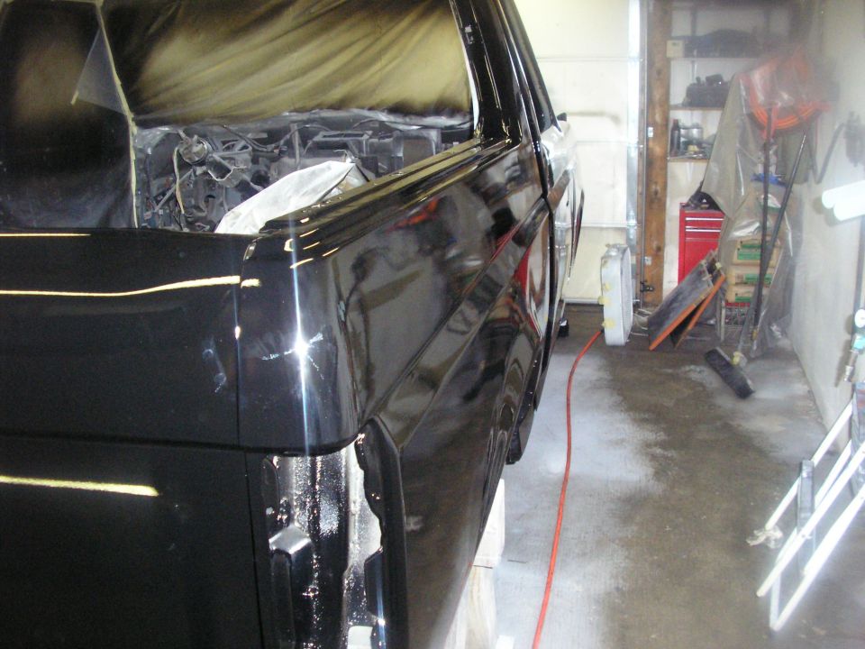 Side view of a black 1987 Ford Bronco being worked on in a garage, with the interior taped off for painting