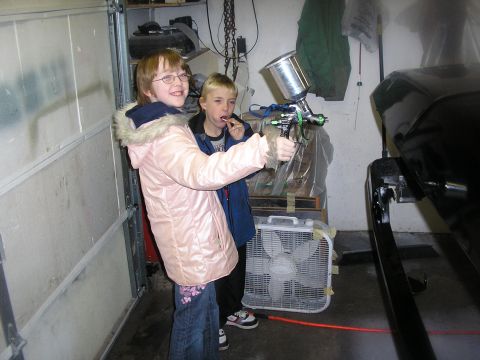 1987 Ford Bronco - Children play with a spray gun in a garage next to a car part.