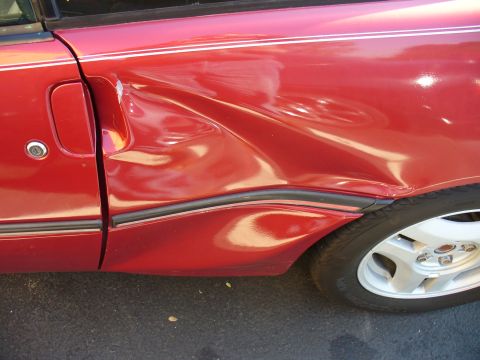 1991 Ford Probe - The side of a red 1991 Ford Probe shows extensive damage to the door and fender area.