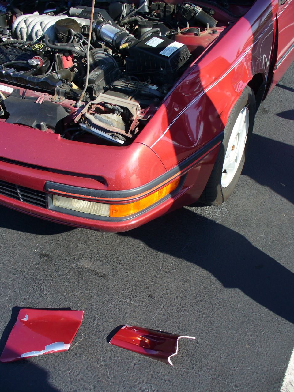 1991 Ford Probe front end with hood open, showing engine and detached bumper pieces on the ground