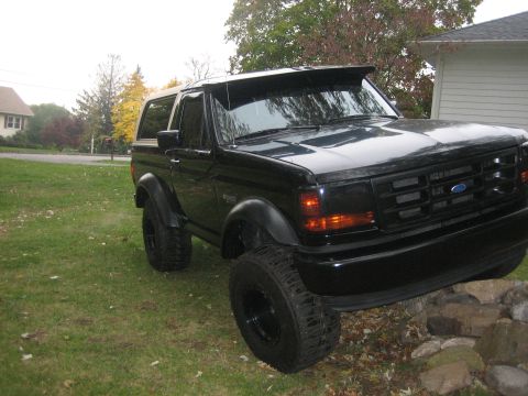 1995 Ford Bronco - This black Ford Bronco is parked on a grassy area with a house and trees visible.