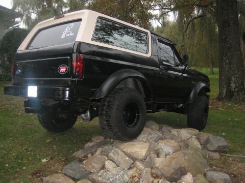 1995 Ford Bronco - This black Ford Bronco with a tan top is lifted and positioned on a pile of rocks.