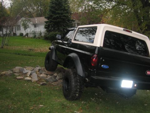 1995 Ford Bronco - Rear view of a black 1995 Ford Bronco with a white removable top, parked on rocks.