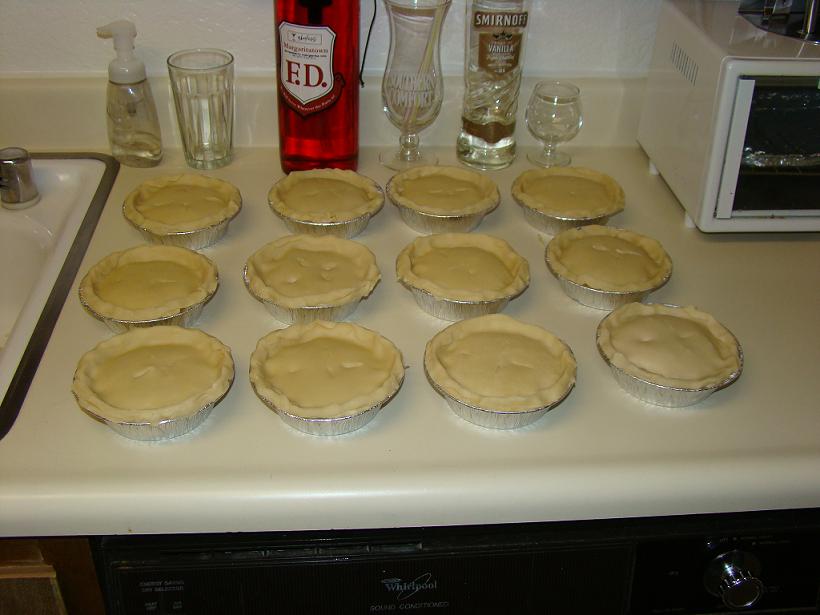 Twelve unbaked pies on a kitchen counter next to bottles of alcohol
