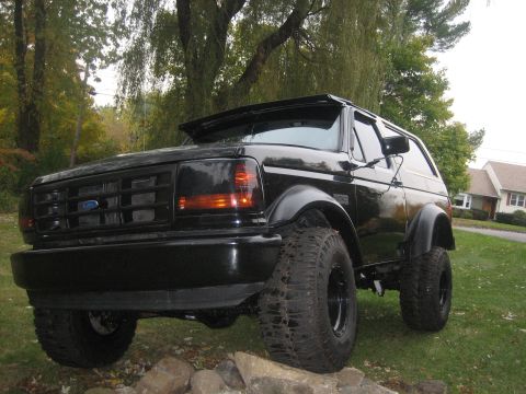 1995 Ford Bronco - This black Ford Bronco is parked on rocks with a suburban house in the background.