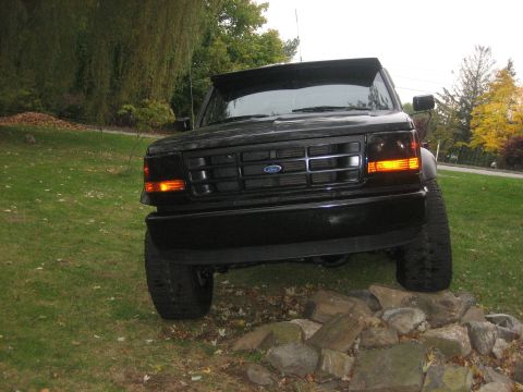1995 Ford Bronco - This black Ford Bronco is parked on a pile of rocks in a grassy area with trees in the background.