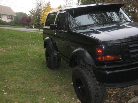 1995 Ford Bronco - A black Ford Bronco is shown from a three-quarter front angle, parked on a lawn with a house in the background.