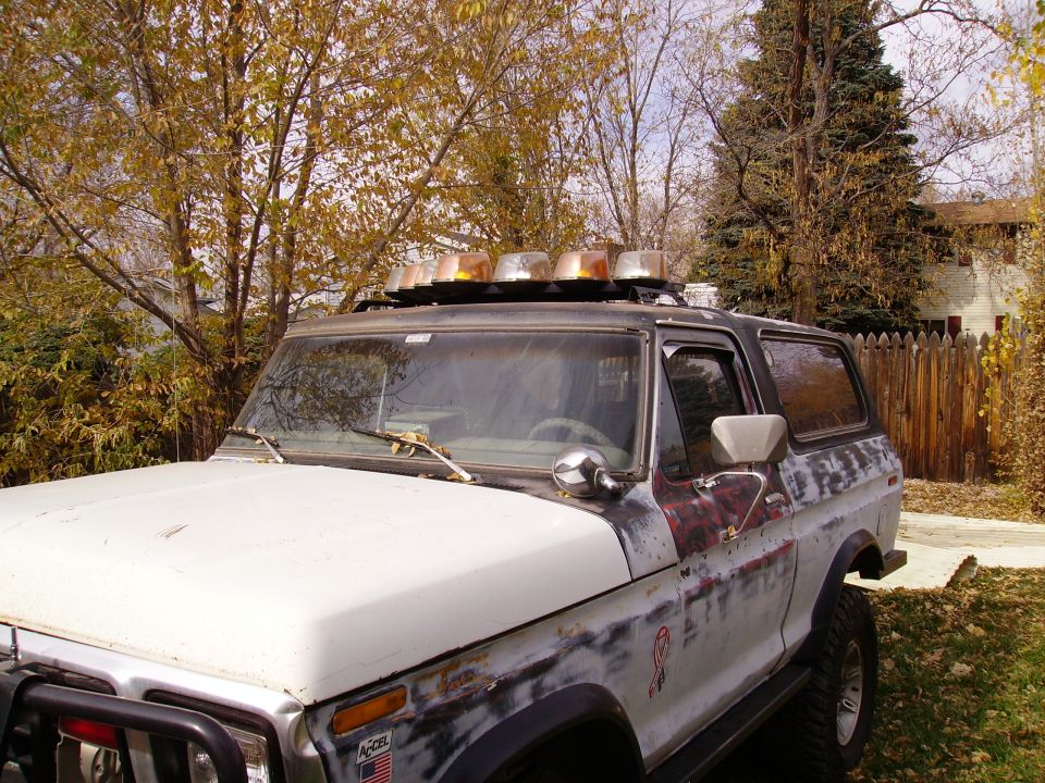 White Ford Bronco with roof lights parked under autumn trees