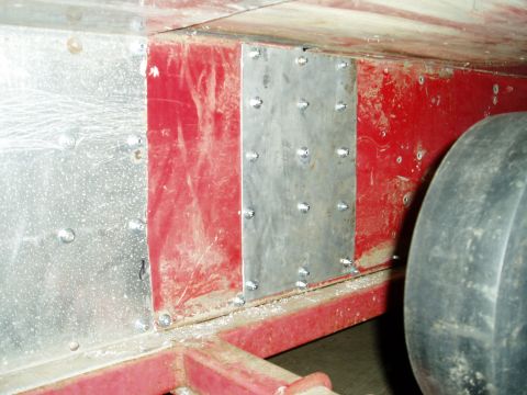 2000 Ford E350 - Close-up view of metal patches riveted onto red bodywork, with a tire visible on the right.