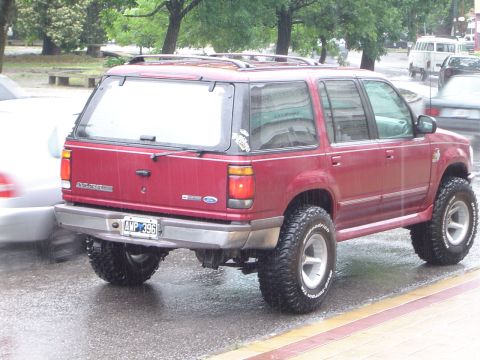 1996 Ford Explorer - Red Ford Explorer SUV with lifted suspension and large tires parked on a wet street.