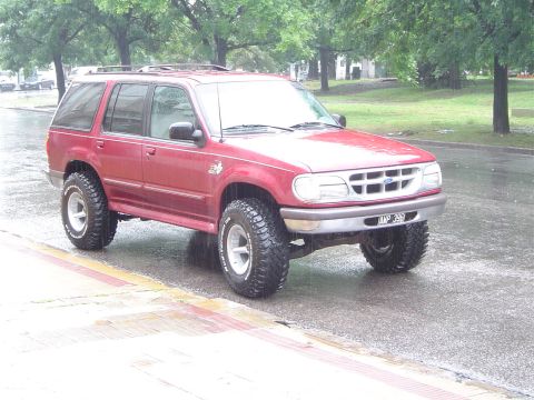 1996 Ford Explorer - A red Ford Explorer SUV is parked on the side of a street during a rain shower.