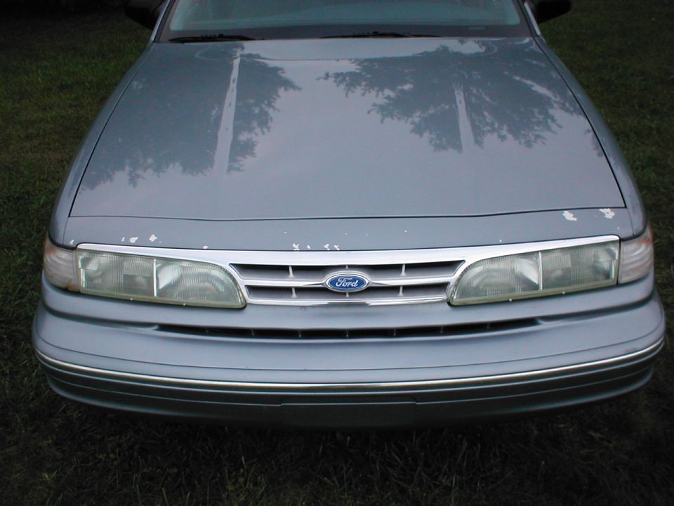 Front end close-up of a light blue-gray Ford sedan with chrome grille, Ford oval and hazed headlights