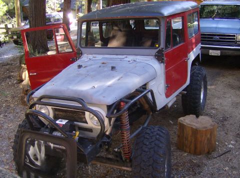 1986 Ford Bronco - Modified Toyota Land Cruiser FJ40 with off-road tires and a winch, parked near a blue Ford truck.