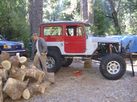 1986 Ford Bronco - A modified off-road vehicle with a red and white body sits next to a pile of logs and another vehicle.