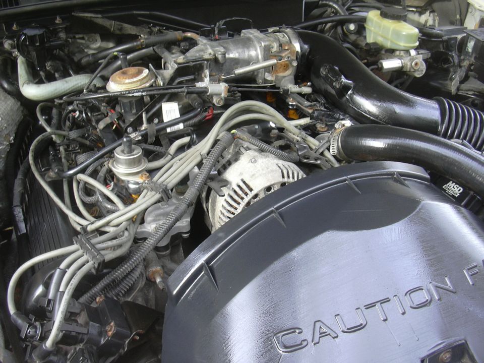 Engine bay with visible wiring, alternator, and black air intake. CAUTION text on cover
