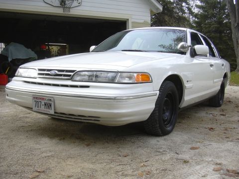 1997 Ford Crown Victoria - A white sedan is parked in front of an open garage door, with a basketball hoop visible above.