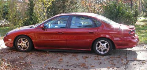 1997 Ford Taurus - This red sedan, likely a 1996 model, is viewed from the side on a leaf-strewn driveway.