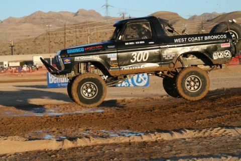 1978 Ford Bronco - Black classic Ford Bronco off-road race truck number 300, West Coast Broncos, catching air on a desert dirt track.