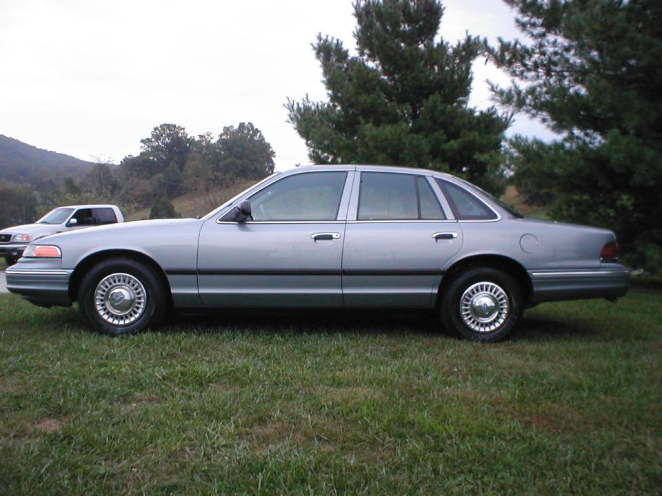 Silver 1997 Ford Crown Victoria sedan, side view. Another vehicle is parked behind it
