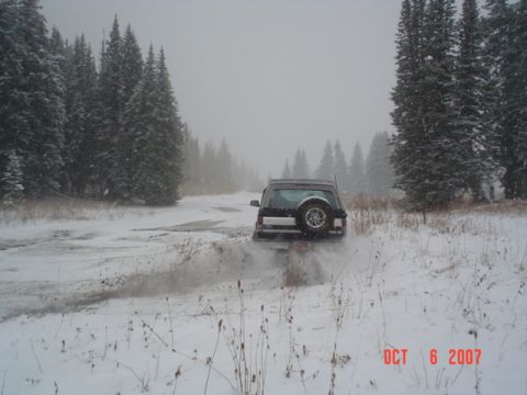 1994 Ford Bronco - An SUV navigates a snow-covered road through a forest on a hazy day.