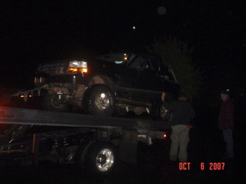 1994 Ford Bronco - A 1994 Ford Bronco is loaded onto a flatbed tow truck in the dark.