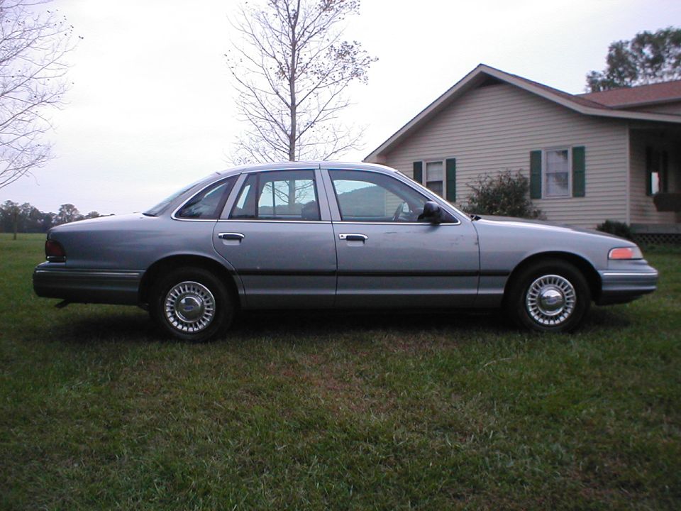 Light blue Ford Crown Victoria sedan in side profile parked on grass