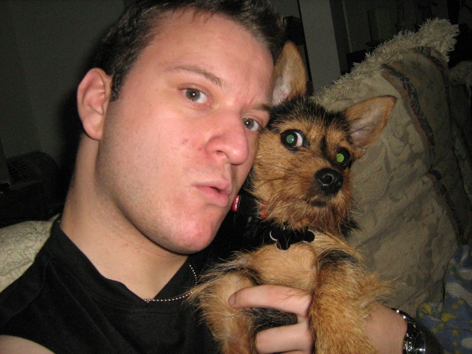 Man in black shirt holding a small brown terrier dog indoors