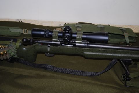 1991 Ford Bronco - A close-up view of a rifle equipped with a scope and bipod, resting on a green fabric surface.