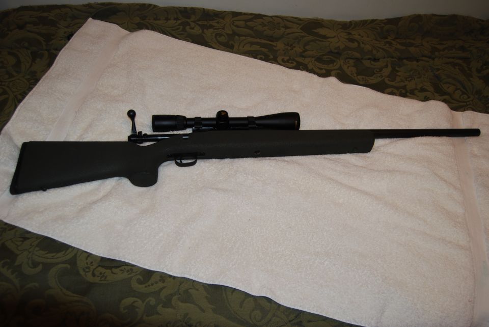 Rifle with a scope mounted on top, resting on a white blanket
