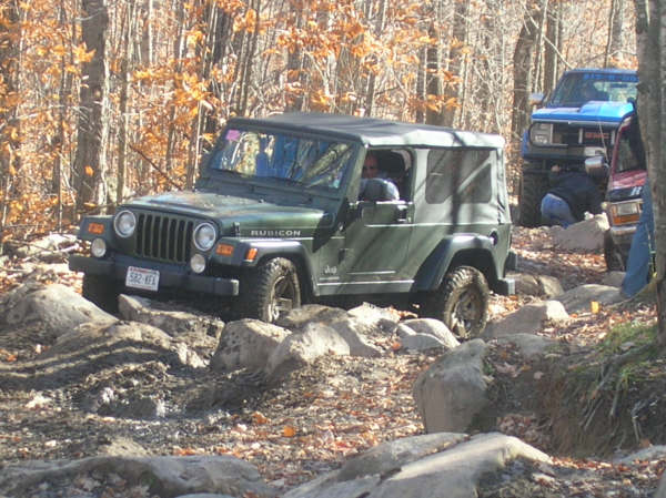 Green Jeep Wrangler Rubicon navigating rocky terrain with other vehicles in background