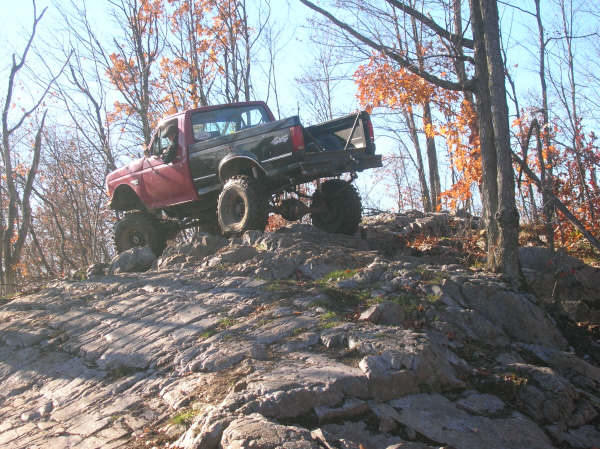 Lifted pickup truck climbing a rocky hill with trees in the background